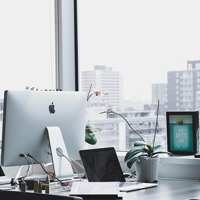 A desk featuring a desktop computer, a laptop, and a small potted plant, creating a productive workspace atmosphere.