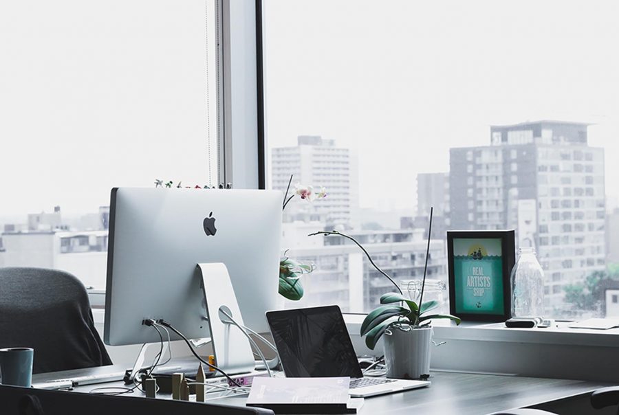 A desk featuring a desktop computer, a laptop, and a small potted plant, creating a productive workspace atmosphere.